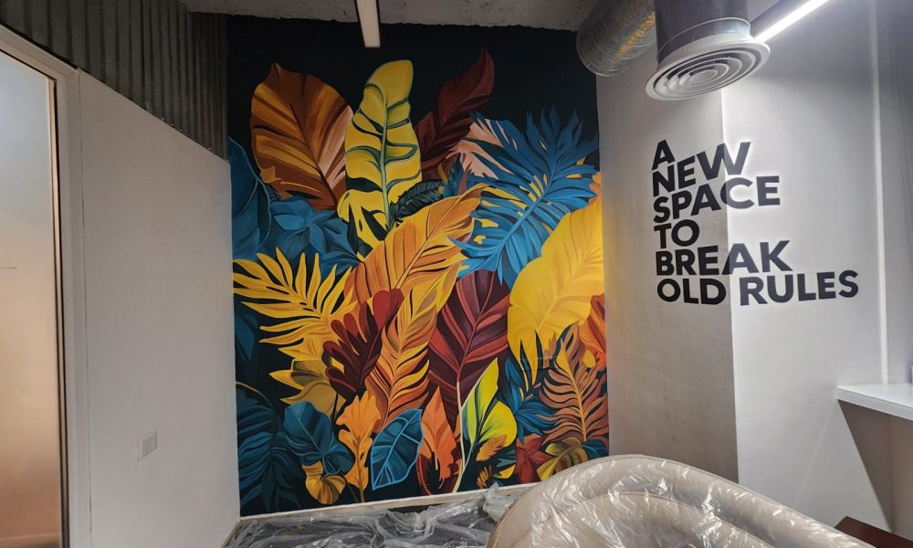 Colorful wall mural with yellow, orange, and blue leaves and the quote “A new space to break old rules” by the Best Wall Painting Artist in Gurgaon.